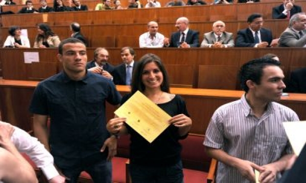 Representante dos estudantes brasileiros exibe diploma na solenidade. Ao fundo, à esq., a pró-reitora de Graduação Cleuza Dias